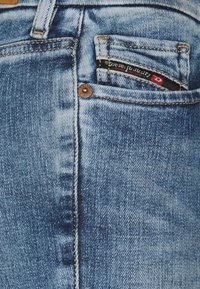 Närbild av en ficka på blå denimjeans med en liten svart och röd Diesel Industry-etikett sydd på myntfickan.
