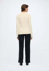 Beige long-sleeve top with a fitted silhouette, paired with black high-waisted trousers. Smooth texture, simple design, no visible hardware.