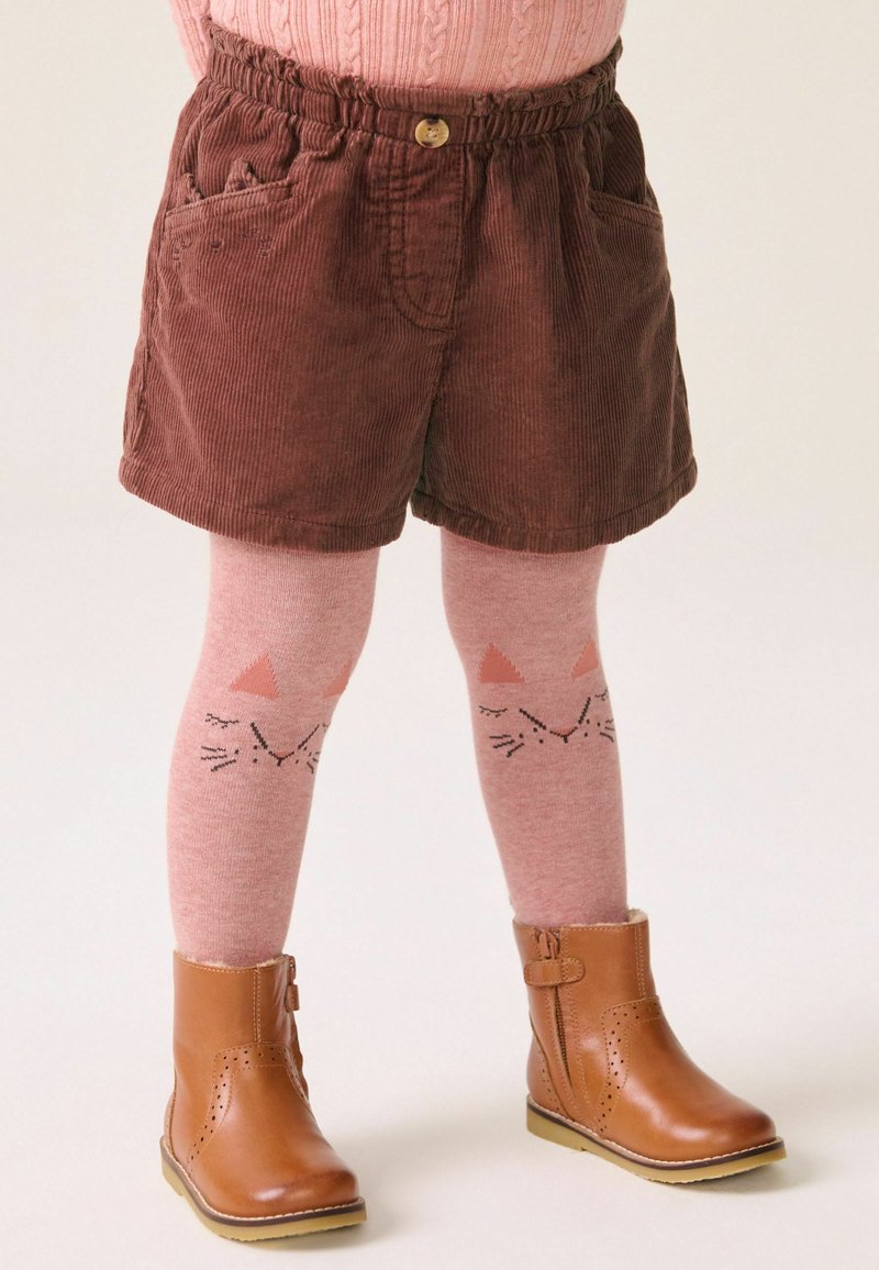 Braune Corduroy-Shorts mit frontalen Taschen, rosa Leggings mit Katzenkopf-Motiven und braune Stiefeletten mit Reißverschlussdetail.