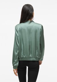 Giubbotto bomber in satin verde spento, con polsini e vita elasticizzati, caratterizzato da una texture liscia e un design minimalista.