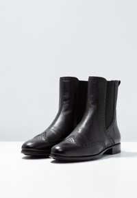 Musta nahkaiset nilkkurit, joissa on sileä pinta, koristeellinen brogue-yksityiskohta, joustavat sivupaneelit ja matala paksu korko.