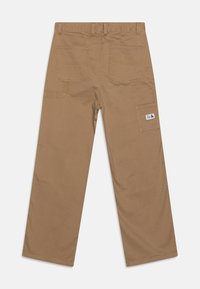 Brune lerretsbukser med rett ben-design, som har to baklommer og en sidelomme, forsterket søm og et lite logo-merke.