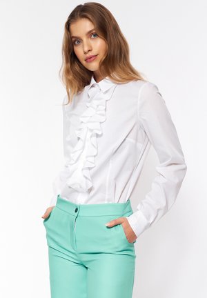 Biała koszula z falbaniastym przodem, długimi rękawami i kołnierzykiem, zestawiona z miętowymi spodniami wykonanymi na miarę z bocznymi kieszeniami i zapięciem na guzik.