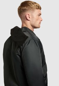 Giacca nera imbottita con cappuccio in fleece nero testurizzato. La giacca ha una finitura liscia e una tasca laterale, che mette in risalto un design moderno.