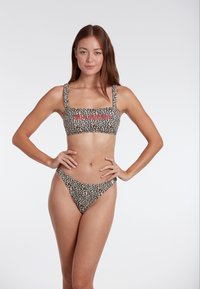 Bikini set s uzorkom leoparda koji uključuje top s kvadratnim izrezom i širokim naramenicama te odgovarajući donji dio s niskim strukom. Tkanina ima mekanu teksturu.