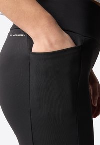 Svarta leggings med en slät, elastisk textur, med en sidoficka och "FLASHDRY"-logotyp på midjan.