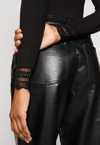 Zwart geribd topje met kanten rand bij de manchetten, gecombineerd met glanzende zwarte leren broek met achterzakken en een gladde textuur.