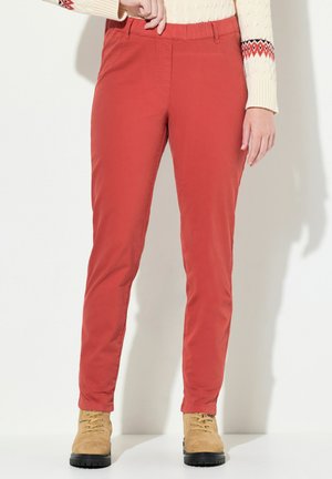 Pantalones ajustados rojos con una textura suave y cinturilla elástica, combinados con botas de cordones color marrón claro. Adecuados para un uso casual o al aire libre.
