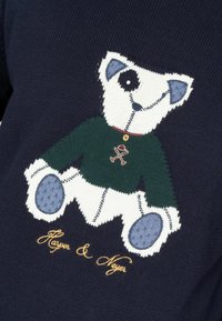 Suéter azul marino con un diseño de oso tejido, una camiseta verde, acentos azules y un logo bordado en dorado "Harper & Meyer" debajo.