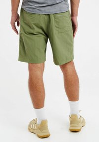 Zelene lagane kratke hlače s opuštenim krojem, s stražnjim džepom i suptilnim logom, uparene s bež sportskim cipelama i bijelim čarapama.