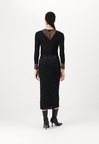 Haut noir à manches longues avec détail en dentelle au dos et aux poignets, associé à une jupe noire ajustée à motif floral et des bottes noires à talons montant jusqu'au genou.