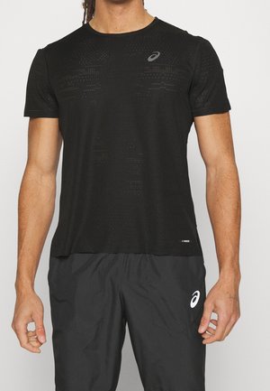 Mann trägt schwarzes perforiertes kurzärmeliges Sportshirt und schwarze Sporthose mit weißen Logos auf Brust und Oberschenkel.