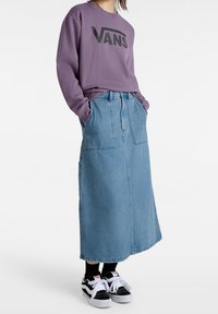 Sudadera morada con el logo negro "VANS", combinada con una falda larga de mezclilla azul que cuenta con bolsillos frontales y zapatillas en blanco y negro.