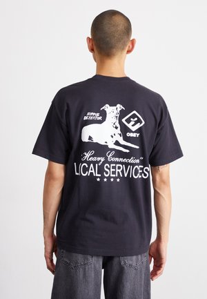 T-shirt en coton noir avec des impressions graphiques blanches d'un chien et de texte. Manches courtes, coupe décontractée, avec un col rond et un ourlet droit.