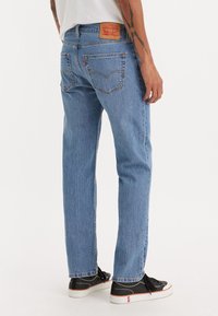 Ljusblå denimjeans med rak passform, som har två bakfickor och en brun läderetikett i midjan. Bärs med svarta skor.