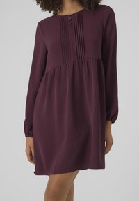 Kurzärmliges, knielanges Kleid in tiefburgunder mit Falten an der Passe und Knopfdetails am Ausschnitt. Glatte Textur, lockere Passform.