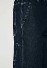 Donkerdenim broek met een relaxte pasvorm, zichtbare witte stiksels en meerdere zakken met een gestructureerde afwerking.