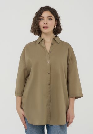 Camicia button-up khaki con vestibilità rilassata, maniche corte e colletto a punta. Texture liscia con bottoni marroni e spacchi laterali.