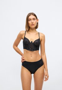 Zwart lingerieset met een transparante beha met gestructureerde cups en verstelbare bandjes, gecombineerd met high-waisted slipjes, beide met stippenpatroon.