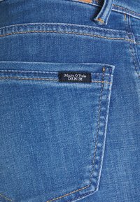 Modré denimové džíny s malou černou etiketou s nápisem "Marc O'Polo DENIM", oranžovými stehy a klasickým designem zadní kapsy.