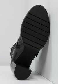 Bota de cuero negro con tacón afilado y suela de goma texturizada, que presenta estrías para tracción y detalles como cremalleras laterales y costuras.