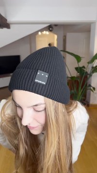 Black knitted beanie with ribbed texture, featuring a square label with "CPH STUDIOS" text on the front. Worn by a person with long hair.
