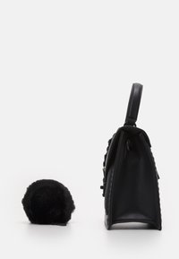 Svart läderhandväska med texturerade sidor, robust handtag och dragkedjeförslutning, bredvid en liten svart faux fur pom-pom-accessoar.
