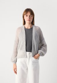 Lichte, open voorkant cardigan in zacht grijs breiwerk, met een gestructureerd patroon en ontspannen mouwen. Gepaard met een grijze top en witte broek.