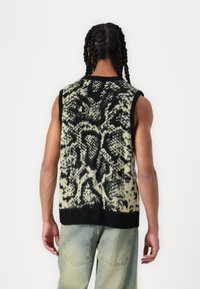 Gebreide mouwloze trui in zwart en room met een gestructureerd abstract patroon. Geribde zoom en ronde halslijn. Casual pasvorm, gecombineerd met lichte denim.