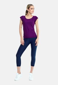Lila kortärmad träningströja med rundad halsringning, ihop med marinblå leggings i ankellängd. Bärs med vita sneakers, slätt tyg, figursydd design.