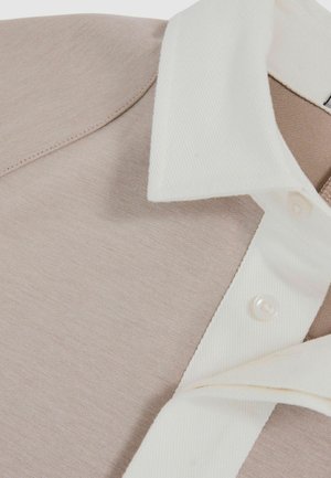 Lys beige poloshirt med en hvid tekstureret krave. Har et glat stof, knaplukning og lige syninger.
