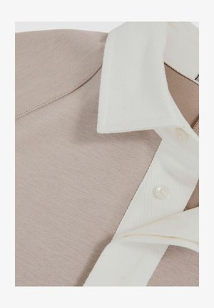 Lys beige poloshirt med en hvid tekstureret krave. Har et glat stof, knaplukning og lige syninger.