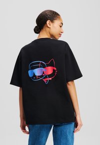 T-shirt en coton noir à coupe décontractée. Présente un graphique d'un personnage et d'un chat portant des lunettes de soleil en bleu et rouge au dos.
