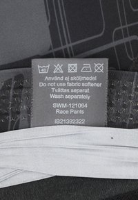 Rennhosen aus schwarzem Stoff mit strukturiertem Muster. Das Pflegeetikett zeigt die Waschhinweise und Produktdetails in Grau.