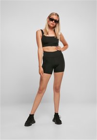 Black sports bra and shorts set, featuring a square neckline, high waistband, and smooth texture, paired with black athletic shoes.