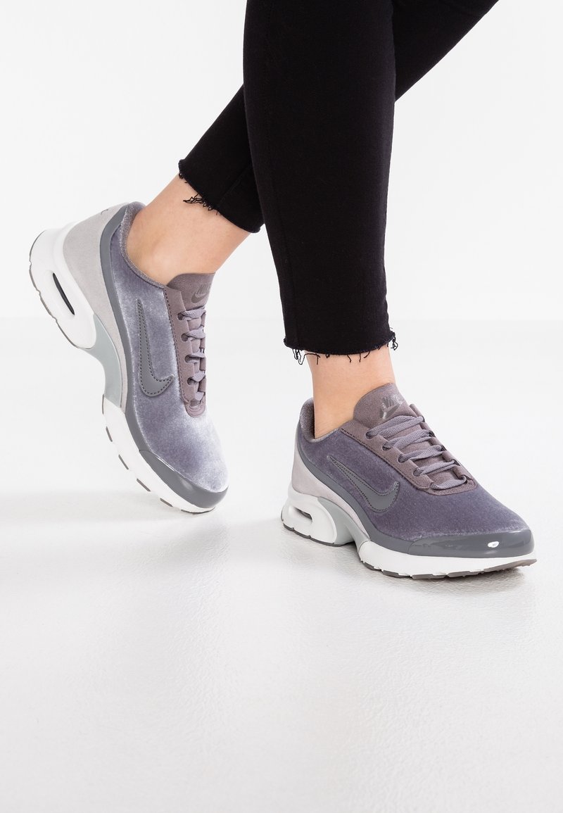 Baskets de sport grises avec un dessus lisse en suède, fermeture à lacets, semelle rembourrée et unité d'air visible. Jean noir avec ourlet effiloché.