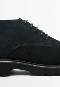 Svarta mocka snörskor med rund tå, texturerad ovandel och gummisula med ett subtilt mönster. Silverfärgade öljett-hål finns.