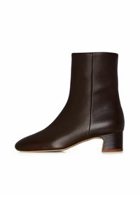 Stivale alla caviglia in pelle marrone con punta tonda e tacco basso a blocco. Presenta una texture liscia e un design minimalista con cuciture laterali.
