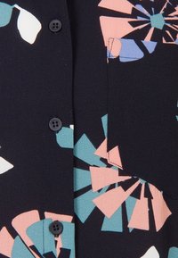 Knapp-up skjorta med en marinblå bakgrund och ett blommönster i rosa, teal och vitt; mjuk textur med synliga knappar och fickdetalj.