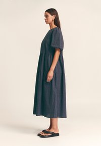 Abito lungo blu navy a balze con maniche a sbuffo, caratterizzato da un motivo sottile di linee verticali colorate, abbinato a infradito nere.