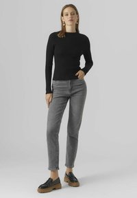 Top negro de manga larga acanalado combinado con jeans de denim gris de cintura alta y zapatos negros tipo slip-on con suela gruesa.