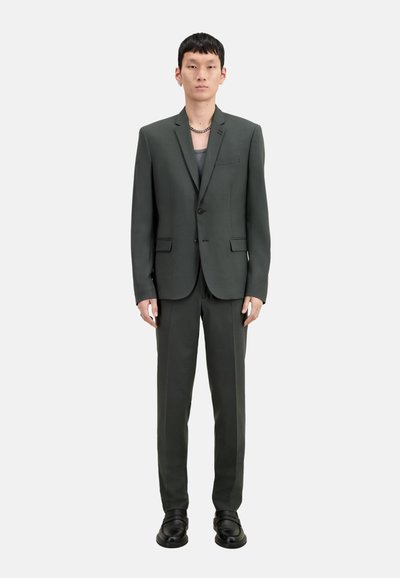 Giacca da giacca verde scuro con due bottoni, pantaloni abbinati e scarpe nere. La giacca ha un colletto a punta e un design slim fit.