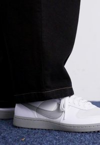 Valged jooksujalatsid halli Nike logo, lame paelu ja tekstureeritud halli tallaga. Kanda koos lahtiste mustade pükstega, mis katavad veidi pahkluude piirkonda.