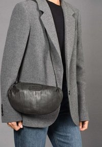 Zwarte leren schoudertas met een ronde vorm; heeft een gladde textuur, een korte schouderband en een klein logo op de voorkant.