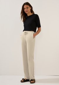 Black short-sleeve top paired with light beige wide-leg pants featuring front pockets and drawstring waist. Black sandals complete the look.