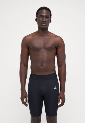 Pantalones cortos deportivos negros hechos de material elástico, con una cinturilla ancha y un pequeño logo blanco de Adidas en el muslo izquierdo.