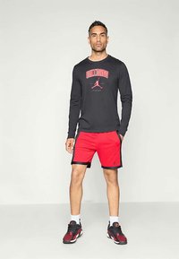 Svart långärmad tröja med en röd "Chicago" grafik, ihopparad med röda shorts med svarta detaljer. Svart och röda sneakers avslutar looken.