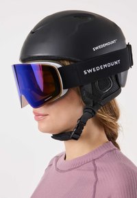 Czarny kask z otworami wentylacyjnymi, wyposażony w szerokie, lustrzane gogle narciarskie z fioletowym gradientem soczewek i regulowanym paskiem. Widoczny logo Swedemount.