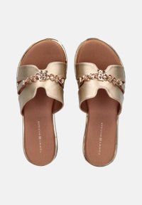 Sandalias de deslizar doradas con detalle de cadena integrado y acento de logo. Parte superior metálica suave, forma redondeada, plantilla acolchada y suela plana.