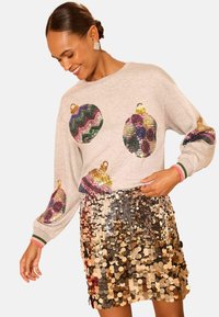 Sudadera gris con diseños ornamentales de lentejuelas coloridas, combinada con una falda brillante de lentejuelas en múltiples tonos, que muestra una vibrante textura y contraste.